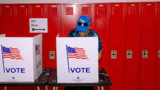 A person votes in a voting booth with an American flag on it in front of red lockers.