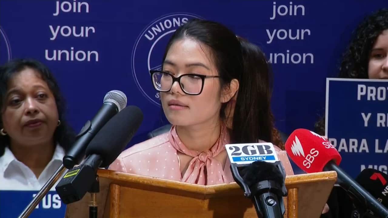 Woman standing at podium surrounded by microphones.