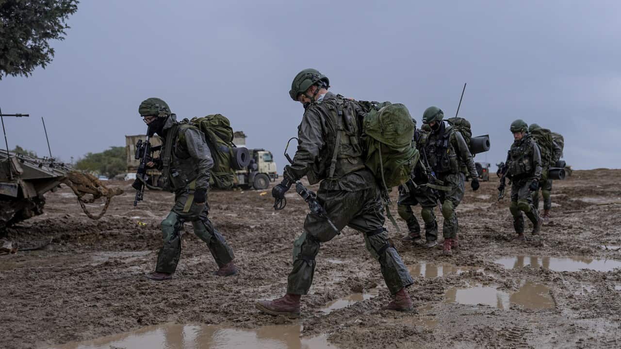 Israeli armed forces walk armed through mud on border of Gaza.