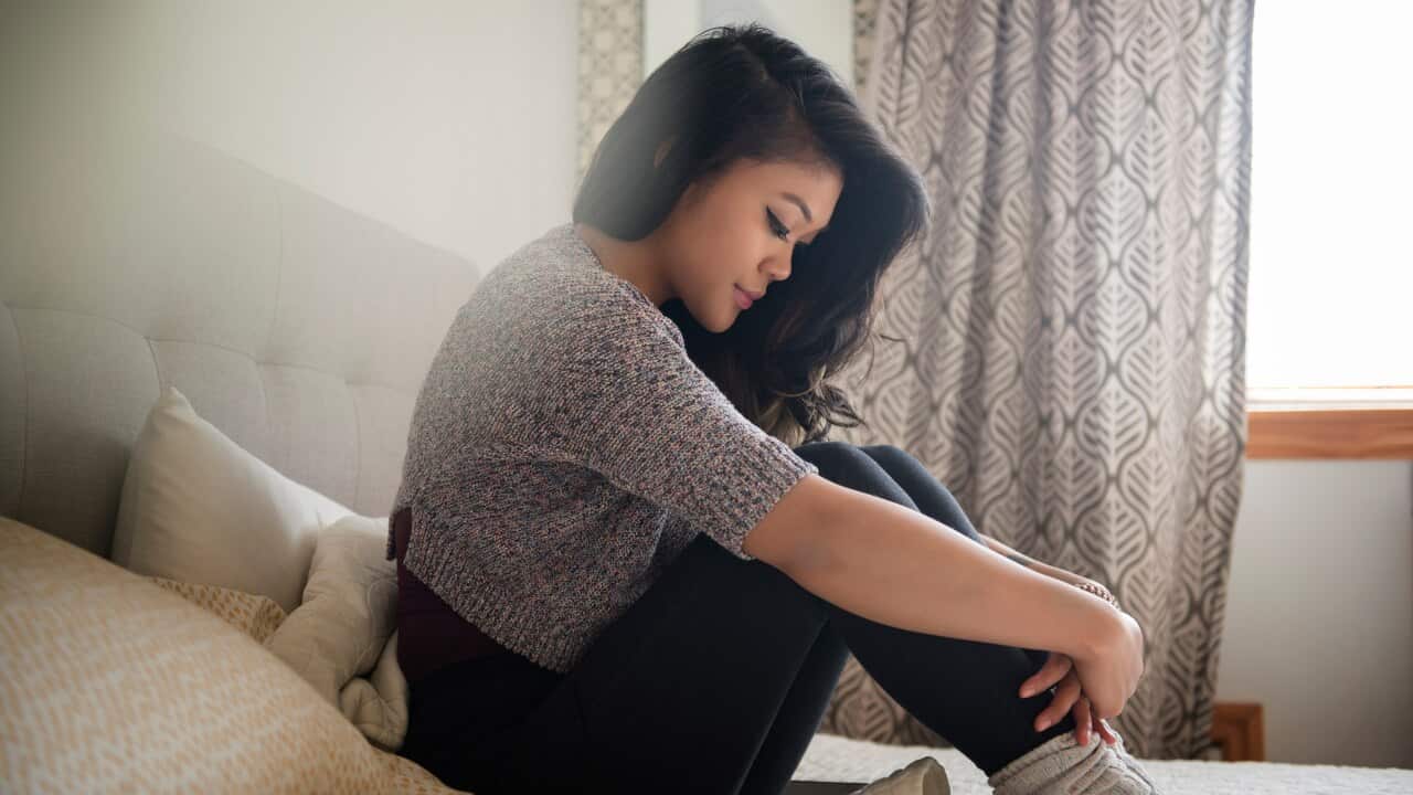 A woman sitting on a bed with a sad expression on her face.