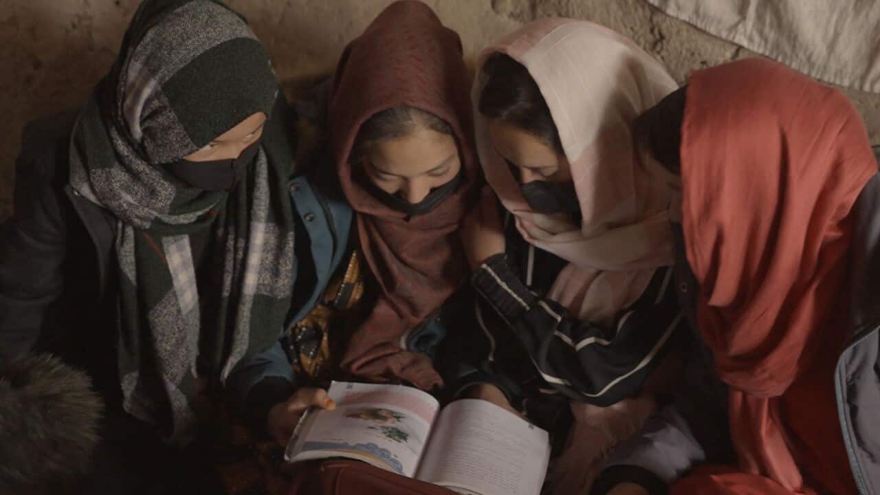 Four teenage girls wearing headscarves and black face masks look closely at an open textbook