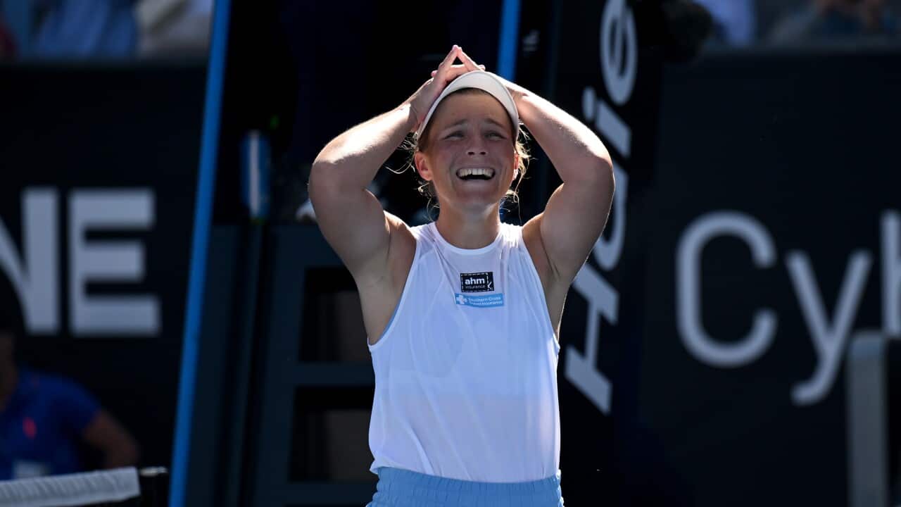 A woman wearing a white singlet and cap stands with her arms on her head and an emotional expression on her face.