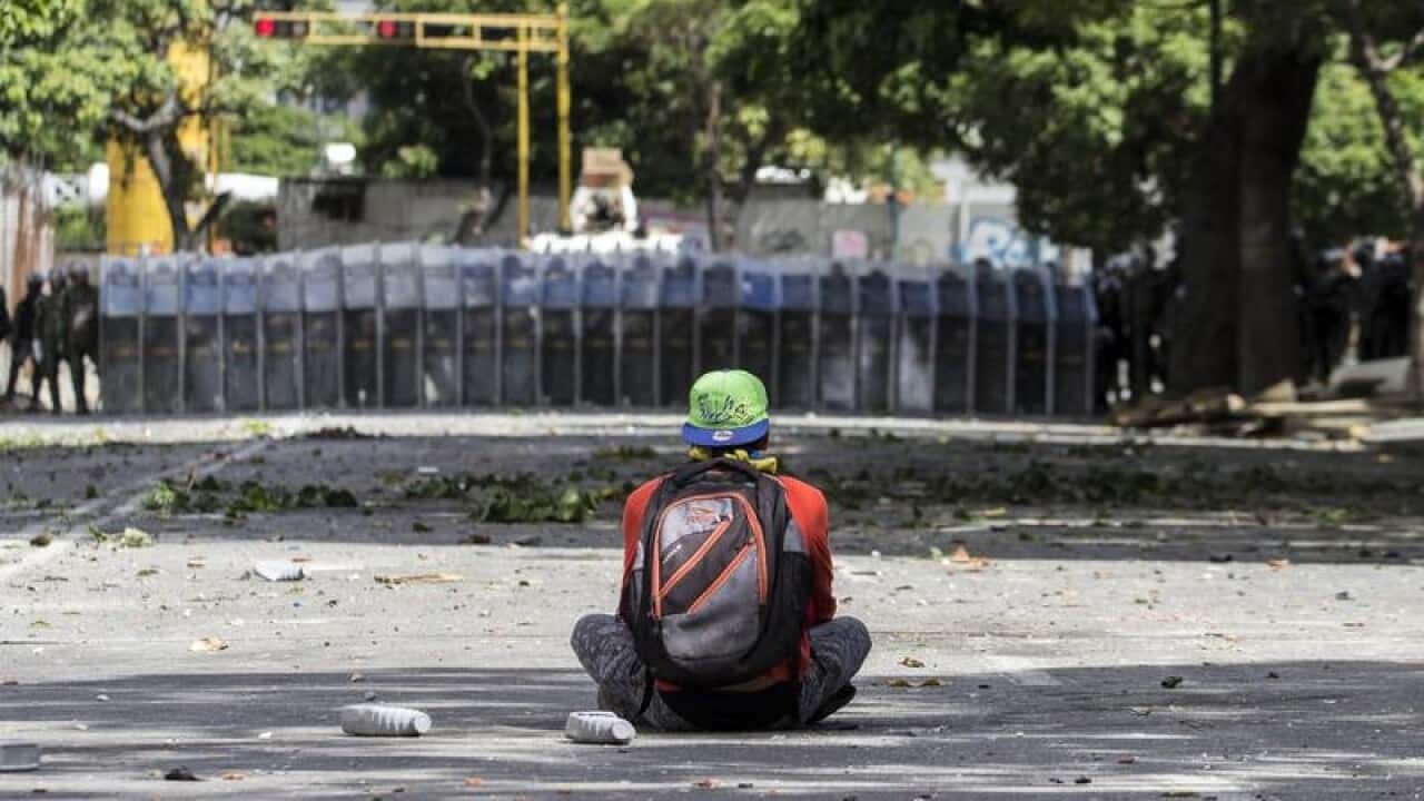 A demonstrator seats in front of a line of Bolivarian National Guard