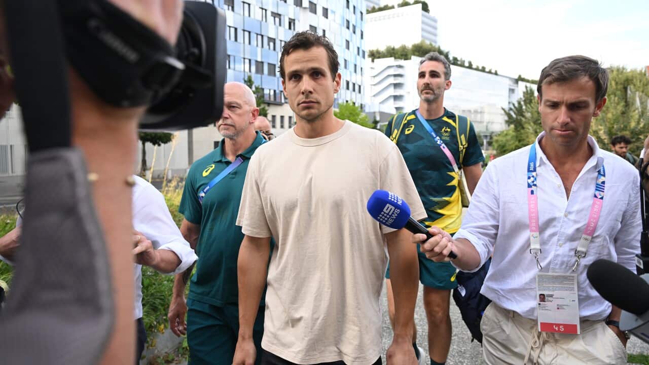 A man in a white shirt stands surrounded by reporters