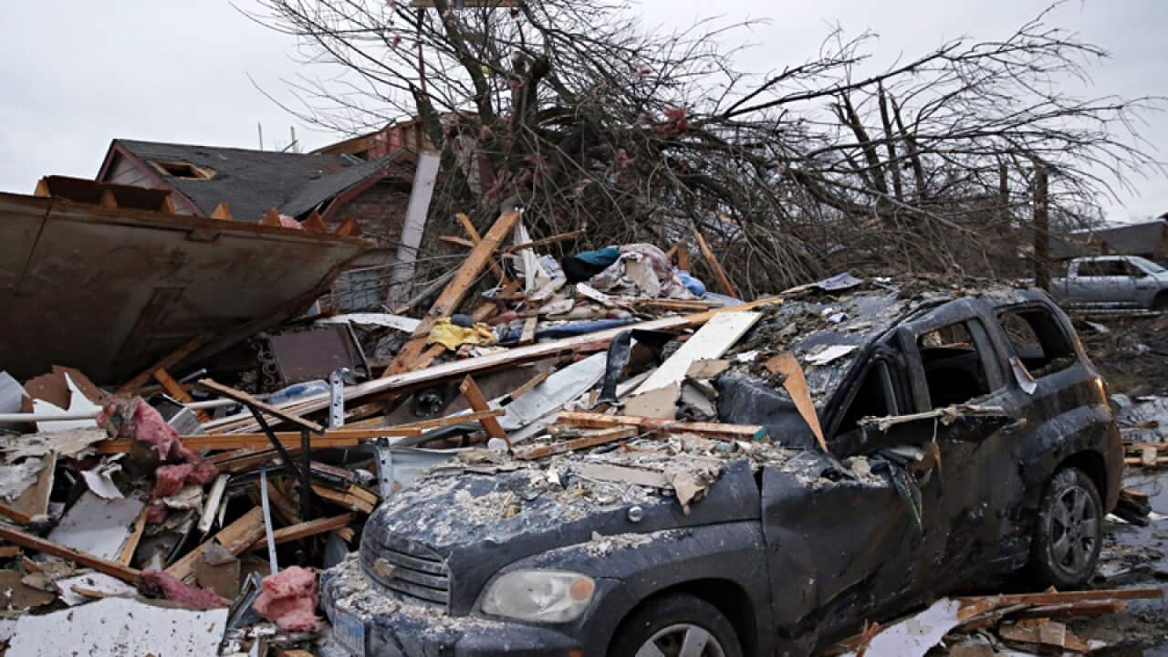 Debris rests on a car in front of a damaged home in Rowlett, Texas