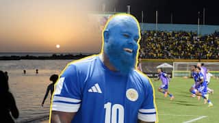 On the left is a beach at sunset. On the right, a team of football players in blue run excitedly. In the centre is a man in a blue kit, his face and beard painted blue, smiling happily.