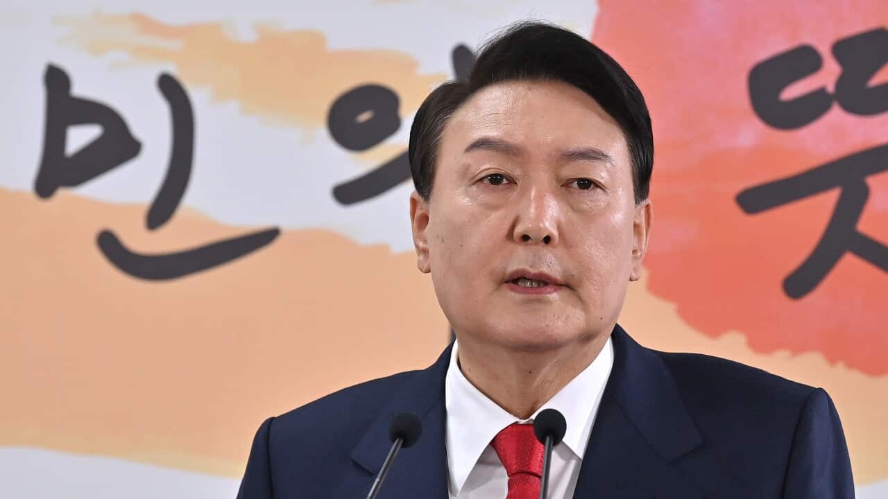 Man wearing suit standing in front of a Korean language billboard.