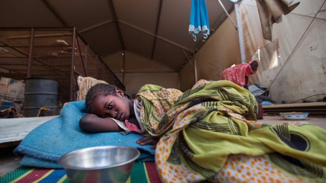 A displaced sick young girl lies under a tent at a mission compound
