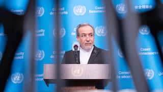 Man speaking at a United Nations podium, viewed through out-of-focus camera equipment, with UN Security Council logos visible on a blue backdrop.