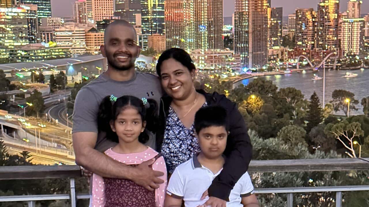 Two adults and their two children smile in front of a cityscape.