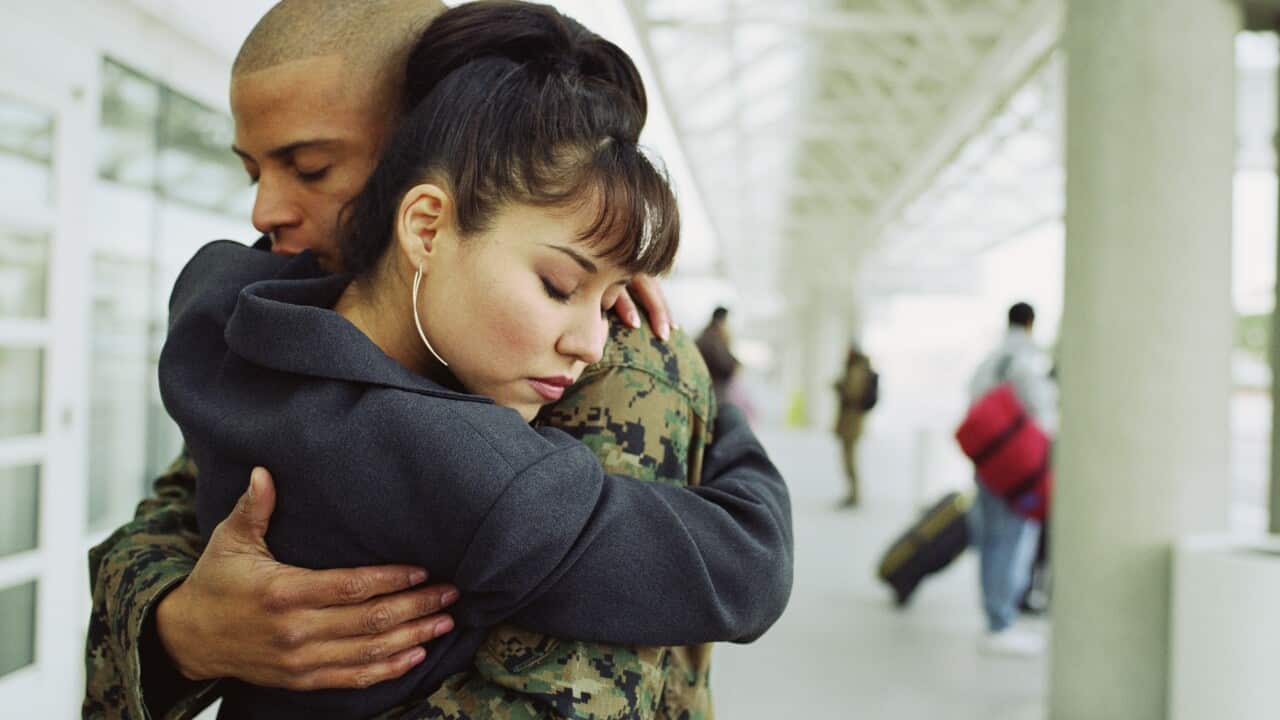 Young couple embracing in airport, man in military uniform