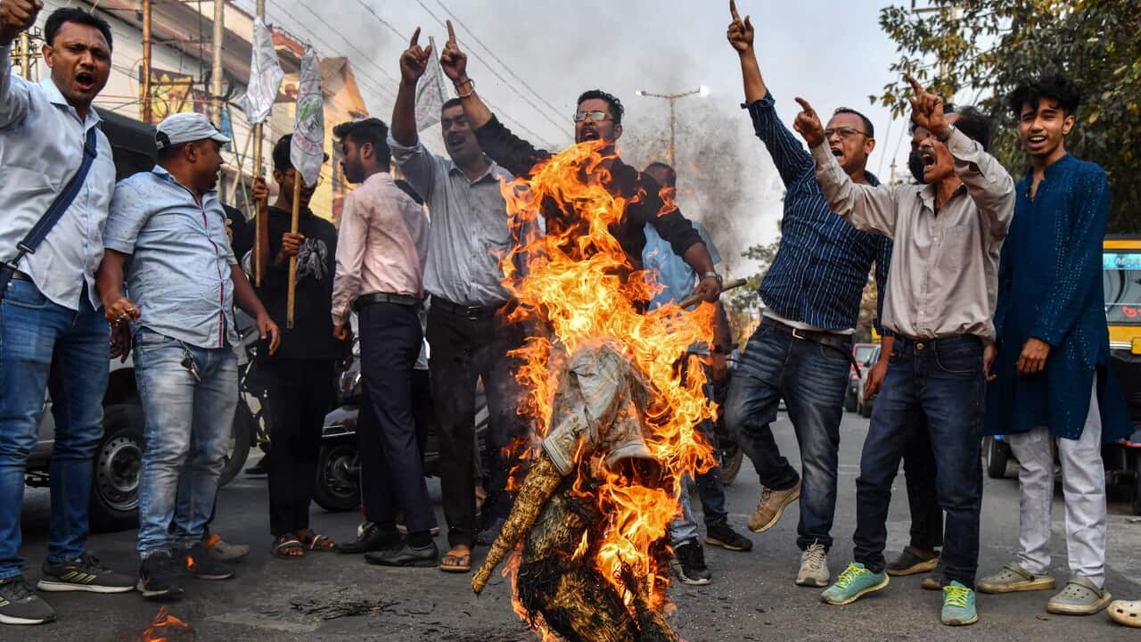 A group of men stand around a burning effigy with their hands raised
