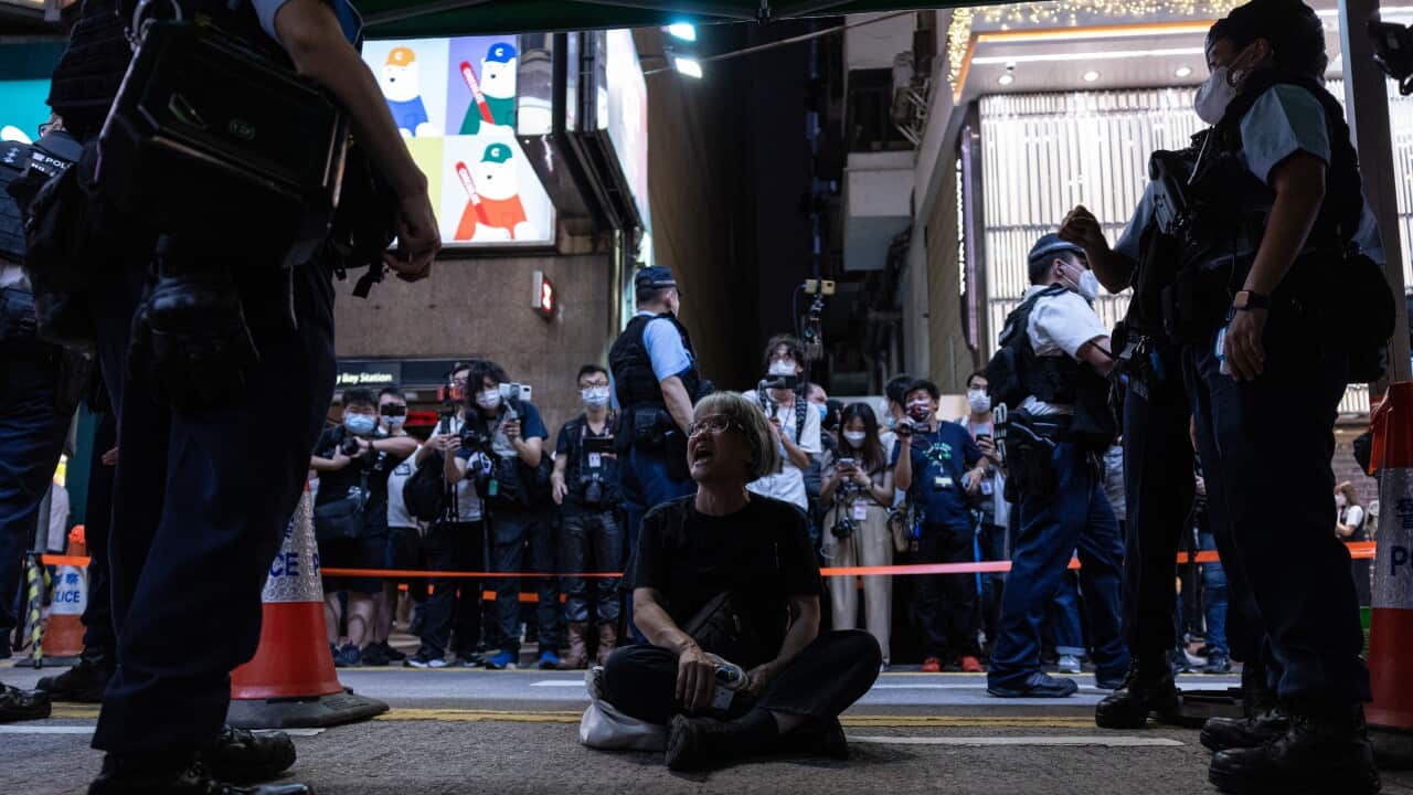 A woman sits on the street as officers look on