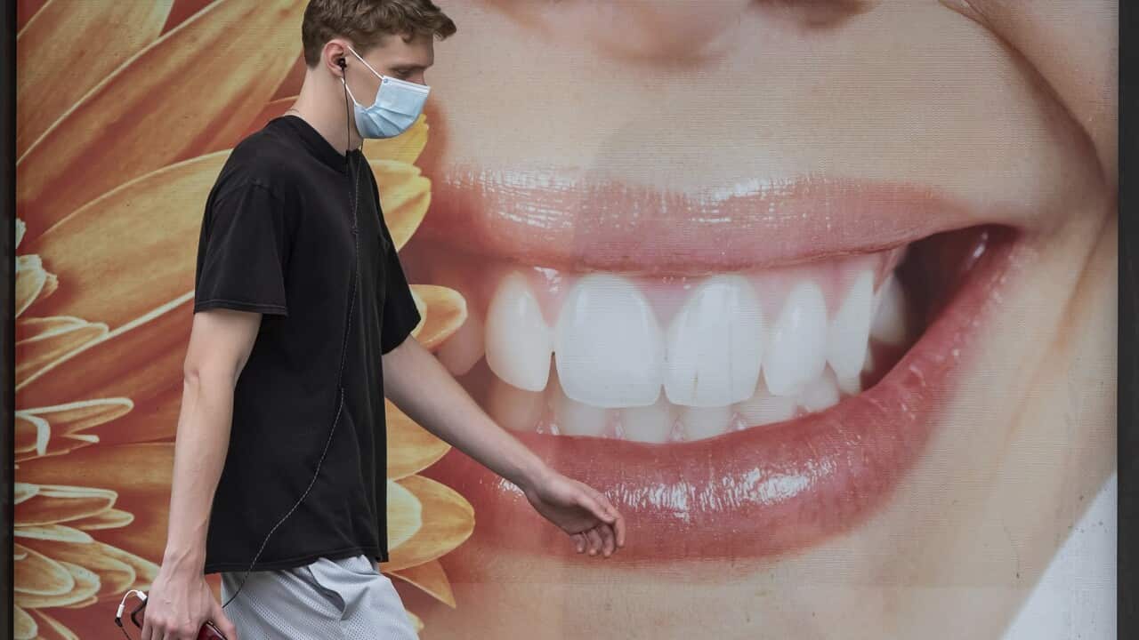 A young man wearing a face mask to curb the spread of COVID-19 walks past a photograph of a woman smiling outside a dental office, in Vancouver, on Monday, August 3, 2020. (Darryl Dyck/The Canadian Press via AP)