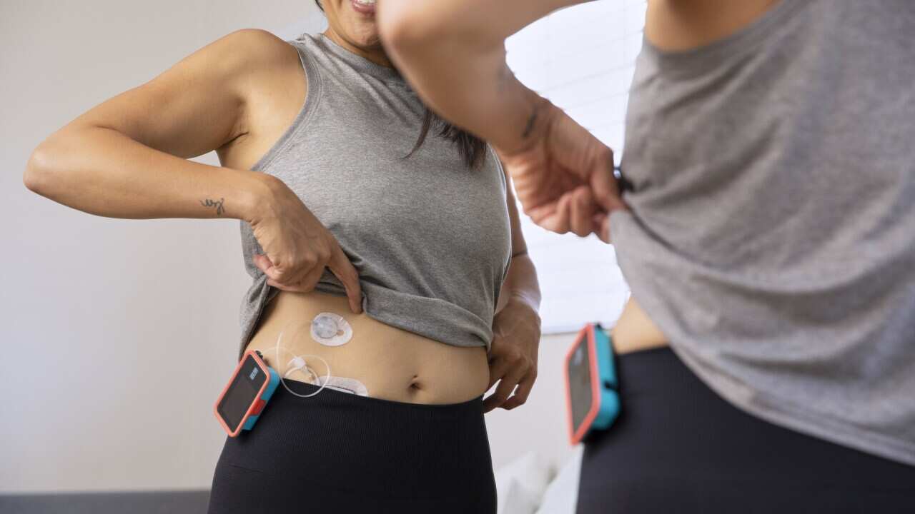 Mirror reflection of woman with type-1 diabetes in workout gear checking her insulin pump and infusion site.