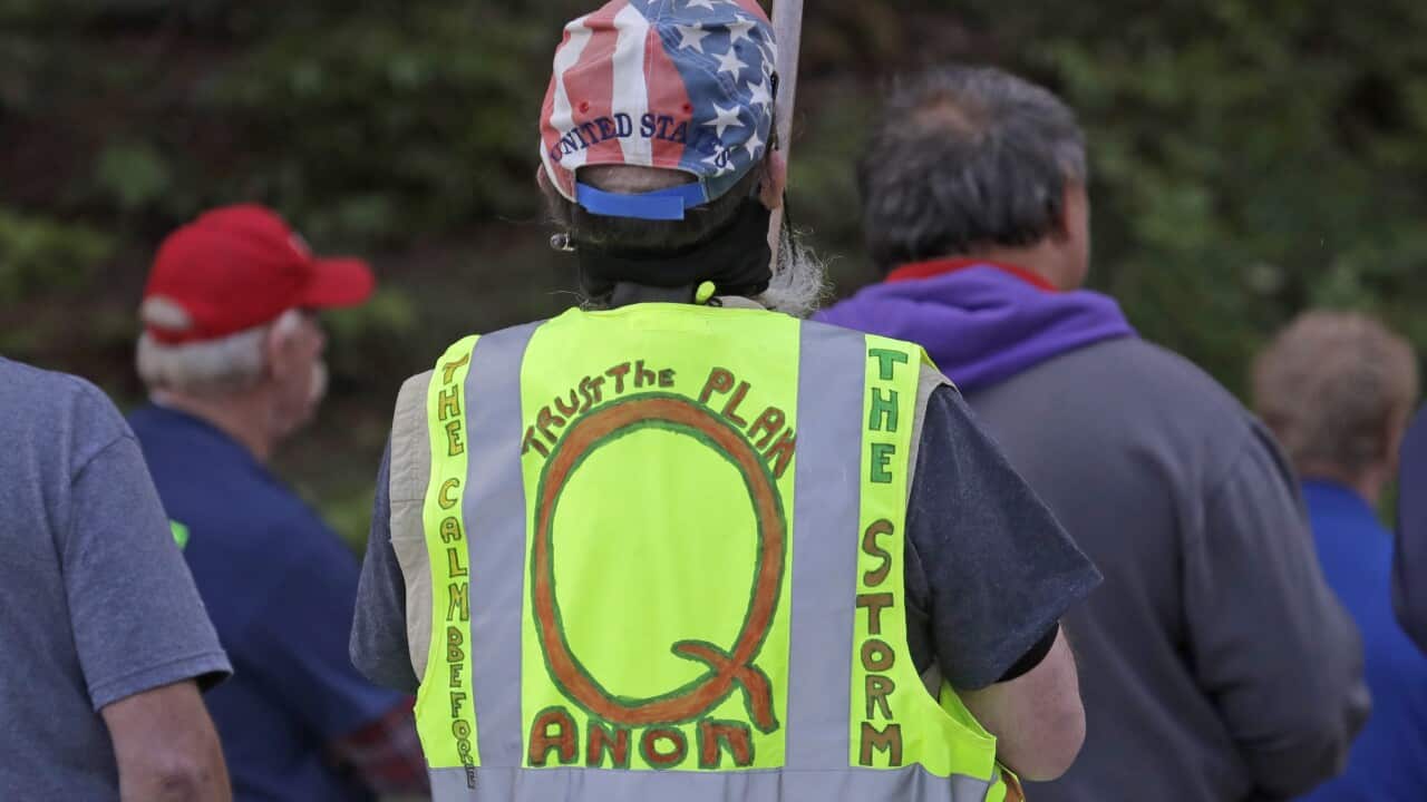 In this May 14, 2020, file photo, a person carries a sign and wears a vest supporting QAnon at a protest in Olympia, Washington
