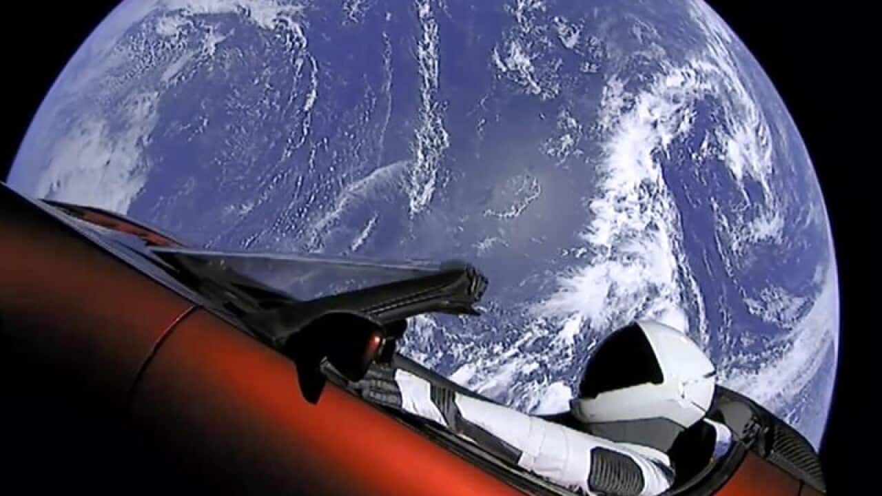 A dummy wearing a spacesuit sits inside a red car in space.