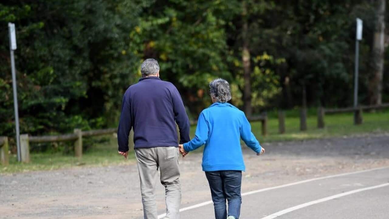 An elderly couple walk through a park