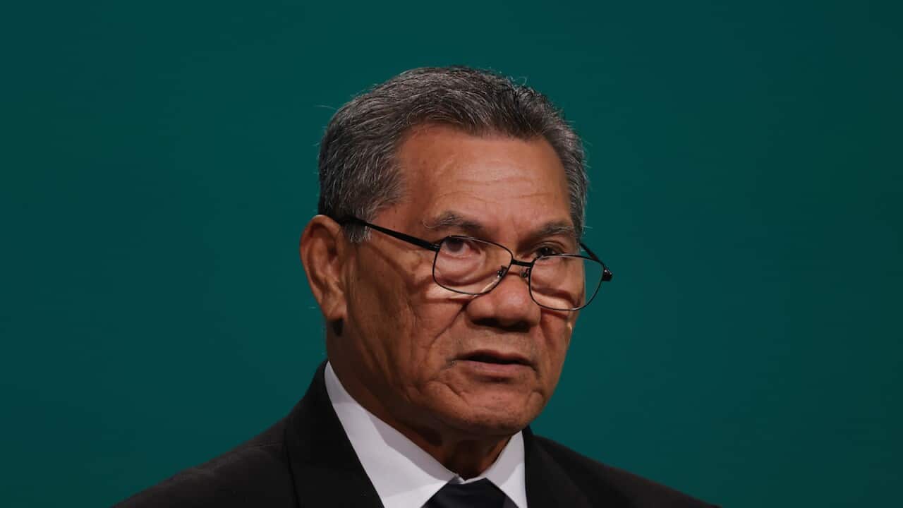 A man wearing glasses standing in front of a teal background.