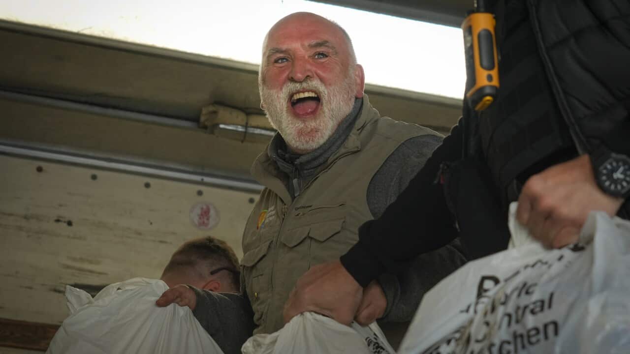 An older man with a beard holding humanitarian food packages and smiling.