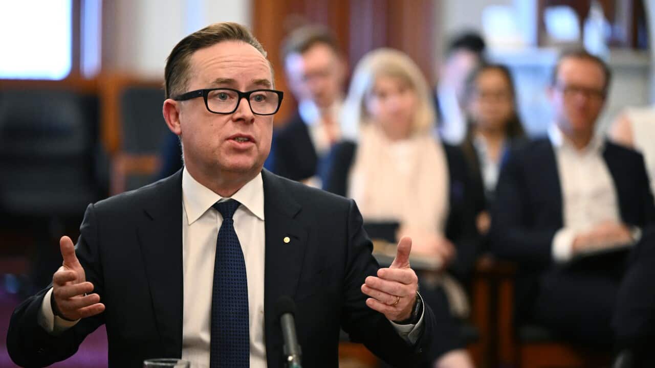 Former Qantas CEO Alan Joyce sitting in a chair with his arms raised while speaking.
