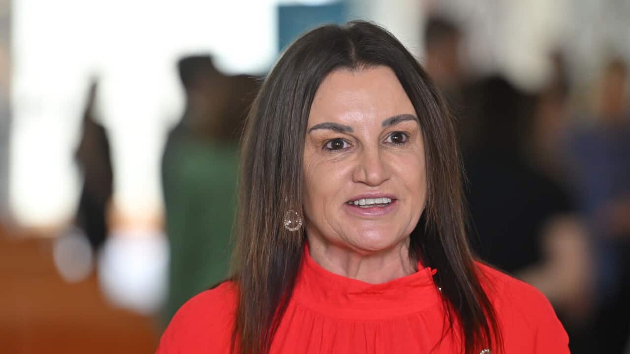 A woman with brown hair wearing a red shirt is speaking.