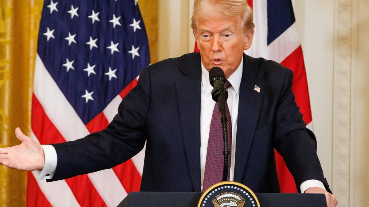 US President Donald Trump, wearing a suit and tie, speaks in front of microphone while standing at a lectern.