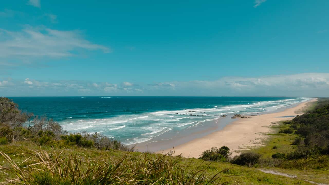 A beach, with gentle waves crashing against the bay, and blue sky in the air.