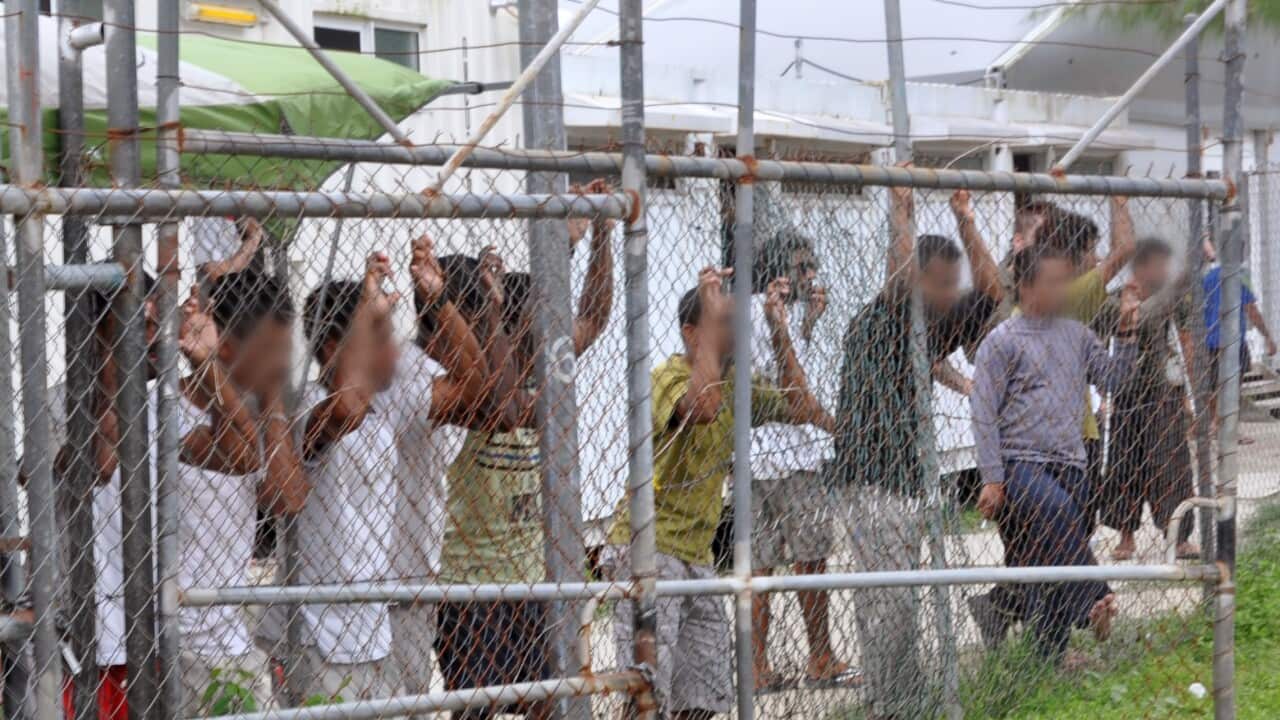 Image of Asylum seekers staring at media from behind a fence at the Oscar compound in the Manus Island detention centre, Papua New Guinea.