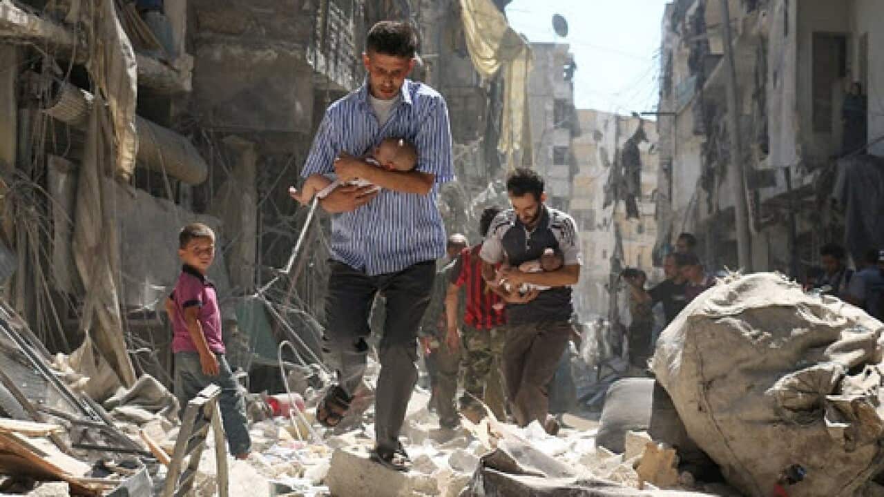 Syrian men carrying babies make their way through the rubble of destroyed buildings following a reported air strike on the rebel-held Salihin neighbourhood.