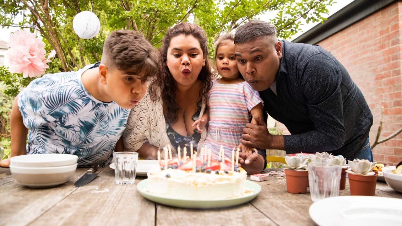Mother, father and two kids blowing out candles on Birthday cake