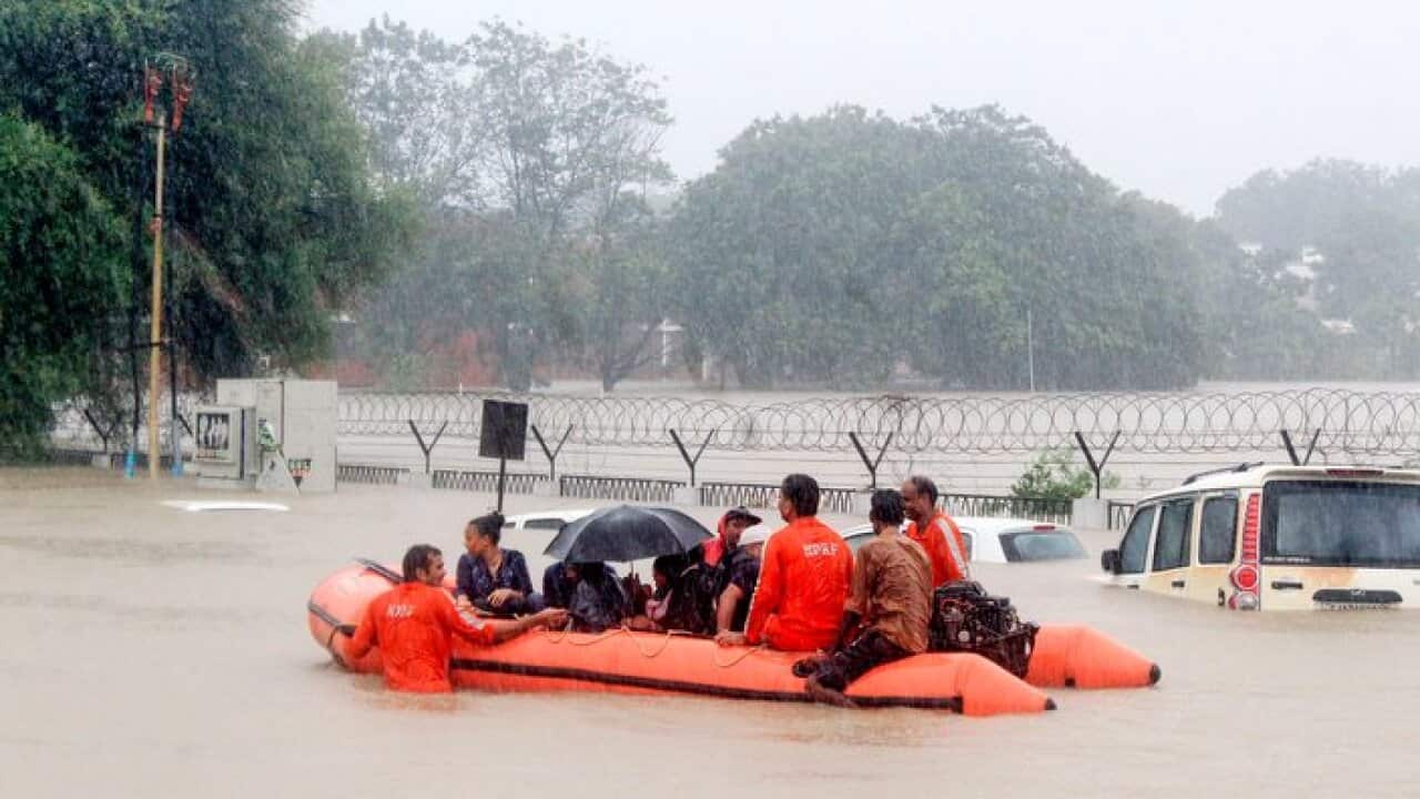 People are being rescued on a boat by personnel from the National Disaster Response Force (NDRF) as they pass by vehicles submerged floodwaters of Vadodara.