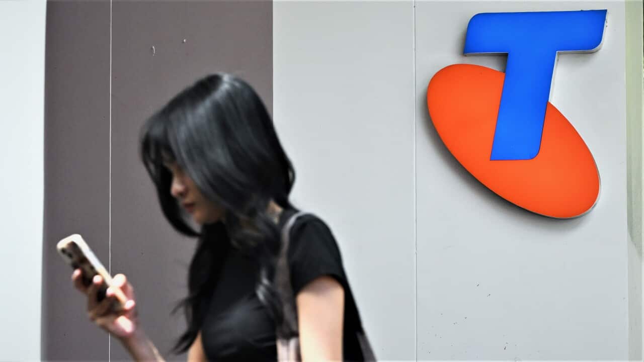 A woman looks at her phone while walking past a Telstra logo.