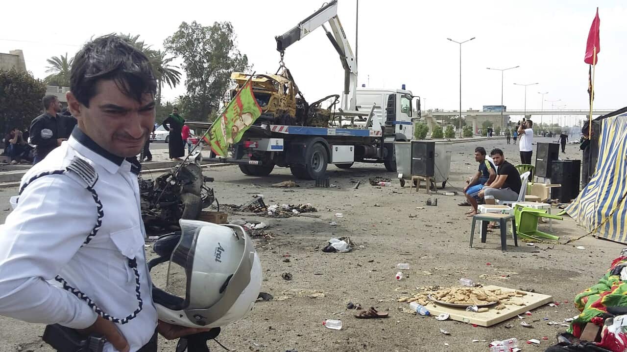 A traffic policeman grieves while security forces prepare to tow away a destroyed car at the scene of a parked car bomb in Baghdad