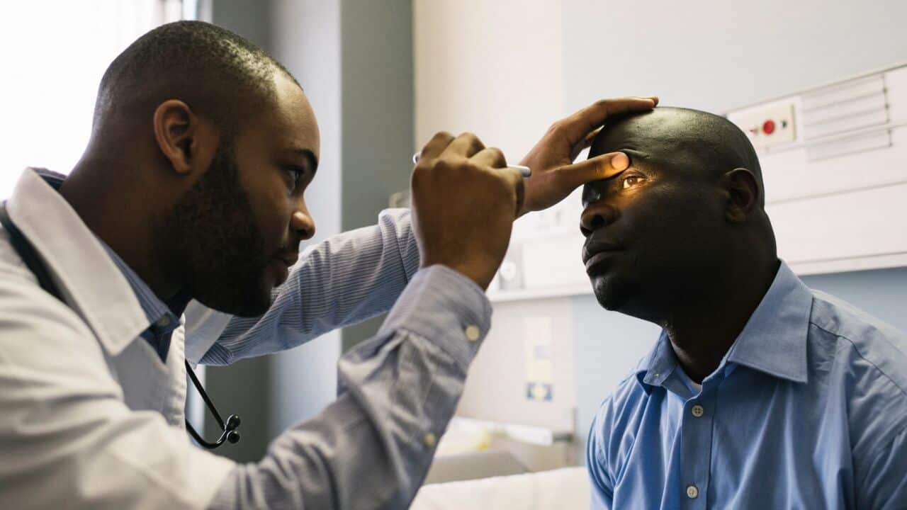 A 50-54 year African male patient's eye examination is done by a young male doctor with an ophthalmoscope Cape Town South Africa