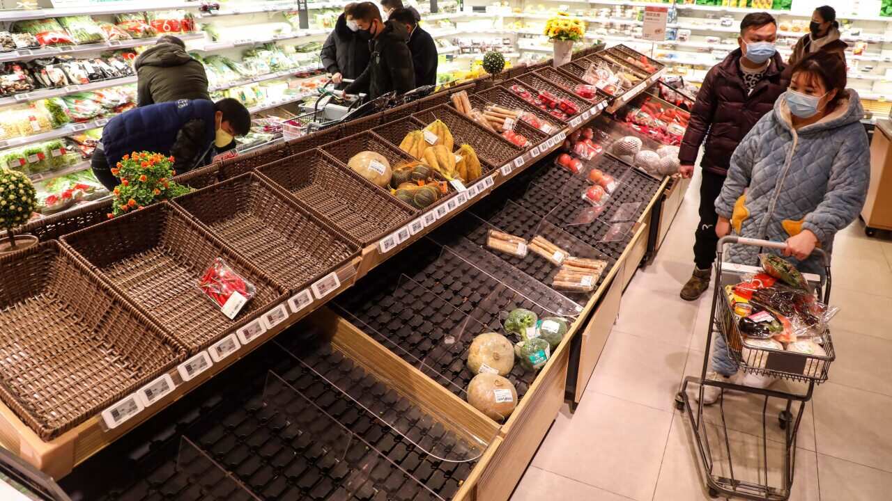 A masked shopper looks at the empty baskets on a counter in a supermarket in Wuhan as locals buy up available food.