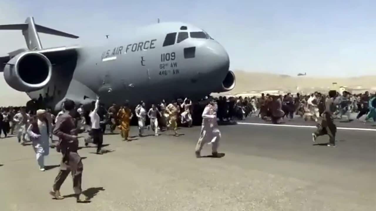 Hundreds of people run alongside a U.S. transport plane as it moves down a runway in Kabul