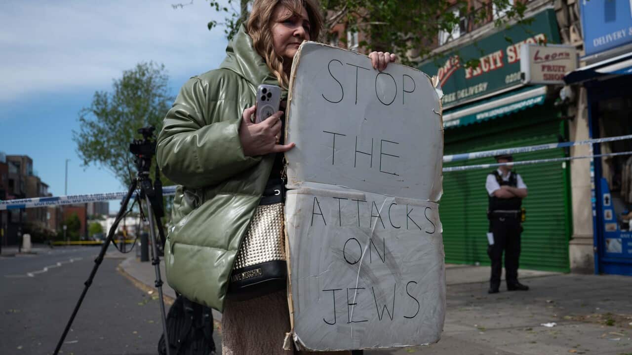 A woman holding a protest sign that says "STOP THE ATTACKS ON JEWS".