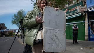 A woman holding a protest sign that says "STOP THE ATTACKS ON JEWS".