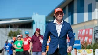 A man wearing a navy suit and an Orange One Nation hat at a polling station