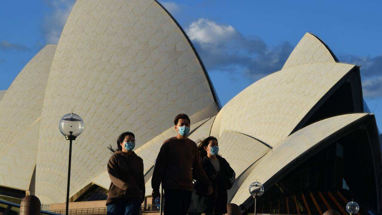 Pedestrians wearing masks walk past the Sydney Opera House.