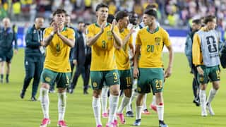 Australian football players in green and gold jerseys clapping a football pitch.