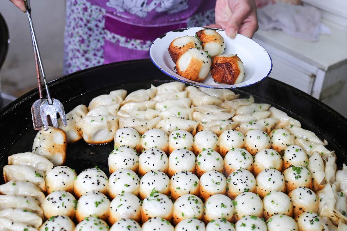Shengjian are crammed tightly into a large pan to cook until their tops are steamed through and their bottoms pan-fried to a delicious crunch.