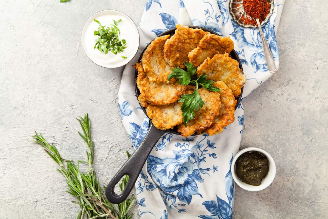 Potato latkes traditional jewish pancakes with sour cream, parsley, dry red pepper flakes and mint sauce. Background, white napkin with blue flowers. Hannukah celebration dish concept. Copy space.
