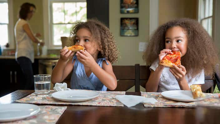 Mixed race girls eating pizza at table
