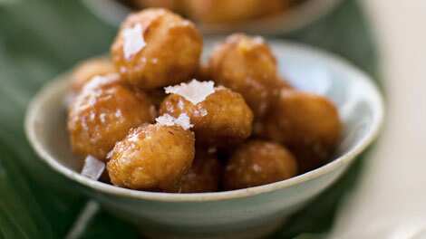 Toffee macadamias sit in a small bowl, with a few flakes of salt on top. 