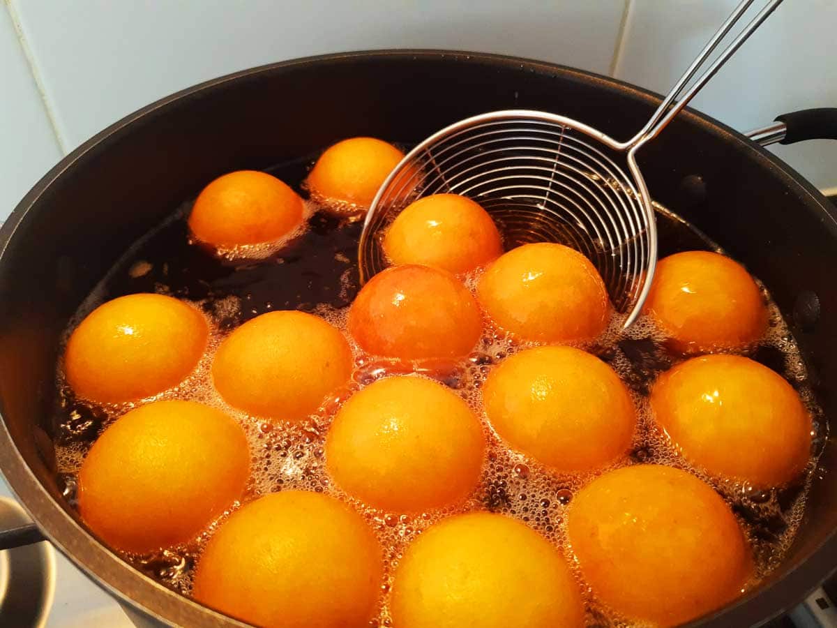 Buñuelos being deep-fried in sizzling oil.
