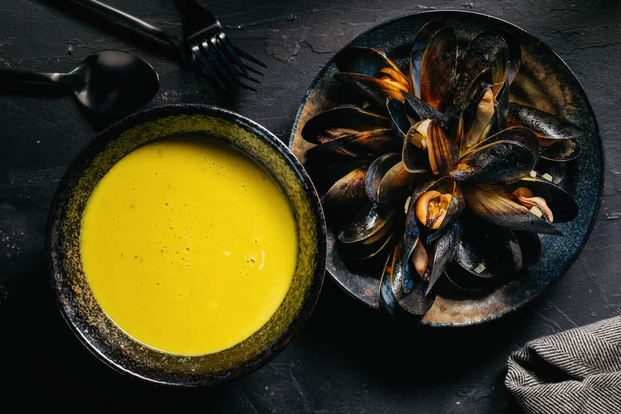 Bowl of yellow broth and a bowl of fresh mussels.