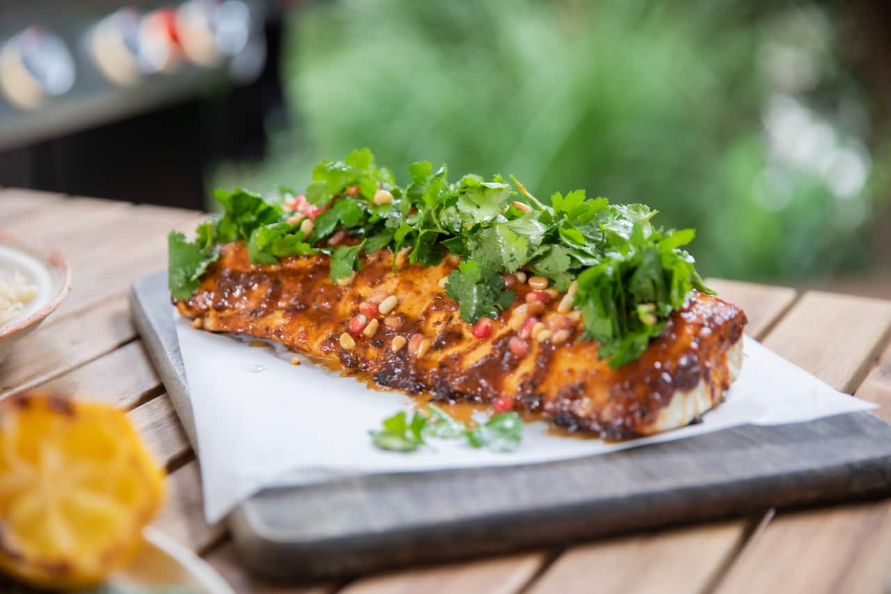 Grilled snapper, harissa, pomegranate, pine nuts & herbs resting on a chopping board, waiting to be served to hungry guests