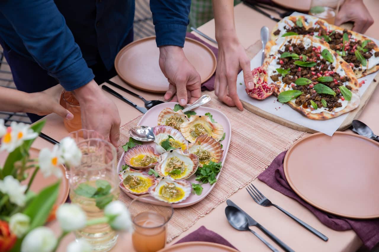 Grilled half shell scallops with green chermoula and buttered almonds being shared amongst guests on a summer entertaining table 